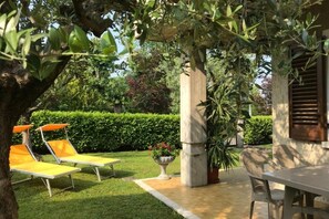 Un jardin avec une table et des chaises, une petite fontaine et une haie en arrière-plan.