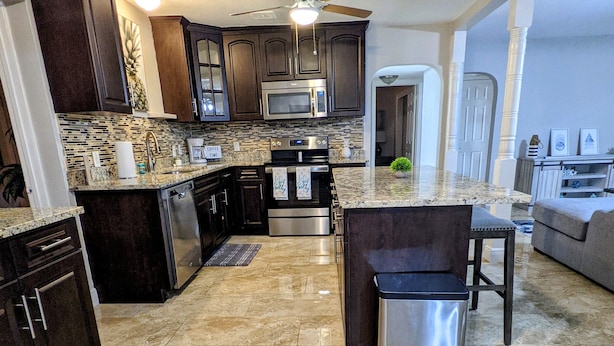 Una cocina moderna con armarios de madera oscura, electrodomésticos de acero inoxidable, encimera de granito y piso de baldosas.