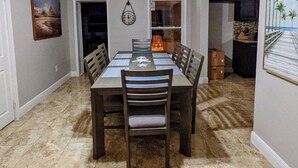 Un comedor con una mesa dispuesta para seis comensales, un ventilador de techo, un reloj y un cuadro en la pared.