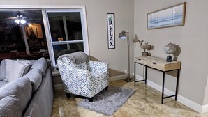 Una sala de estar con un sofá gris, un reposapiés estampado, una mesita con un globo terráqueo y un cuadro en la pared.