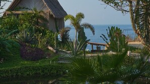 Ein tropisches Resort mit einem Gebäude mit Reetdach, üppiger Vegetation und Blick auf den Ozean.