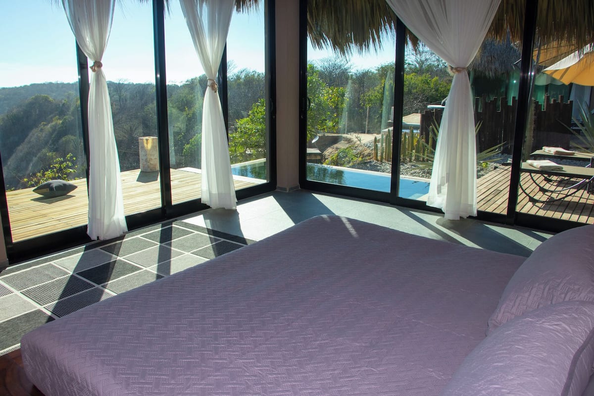 Une chambre dotée d’un grand lit, donnant sur une piscine, et d’une terrasse avec vue sur le paysage environnant.