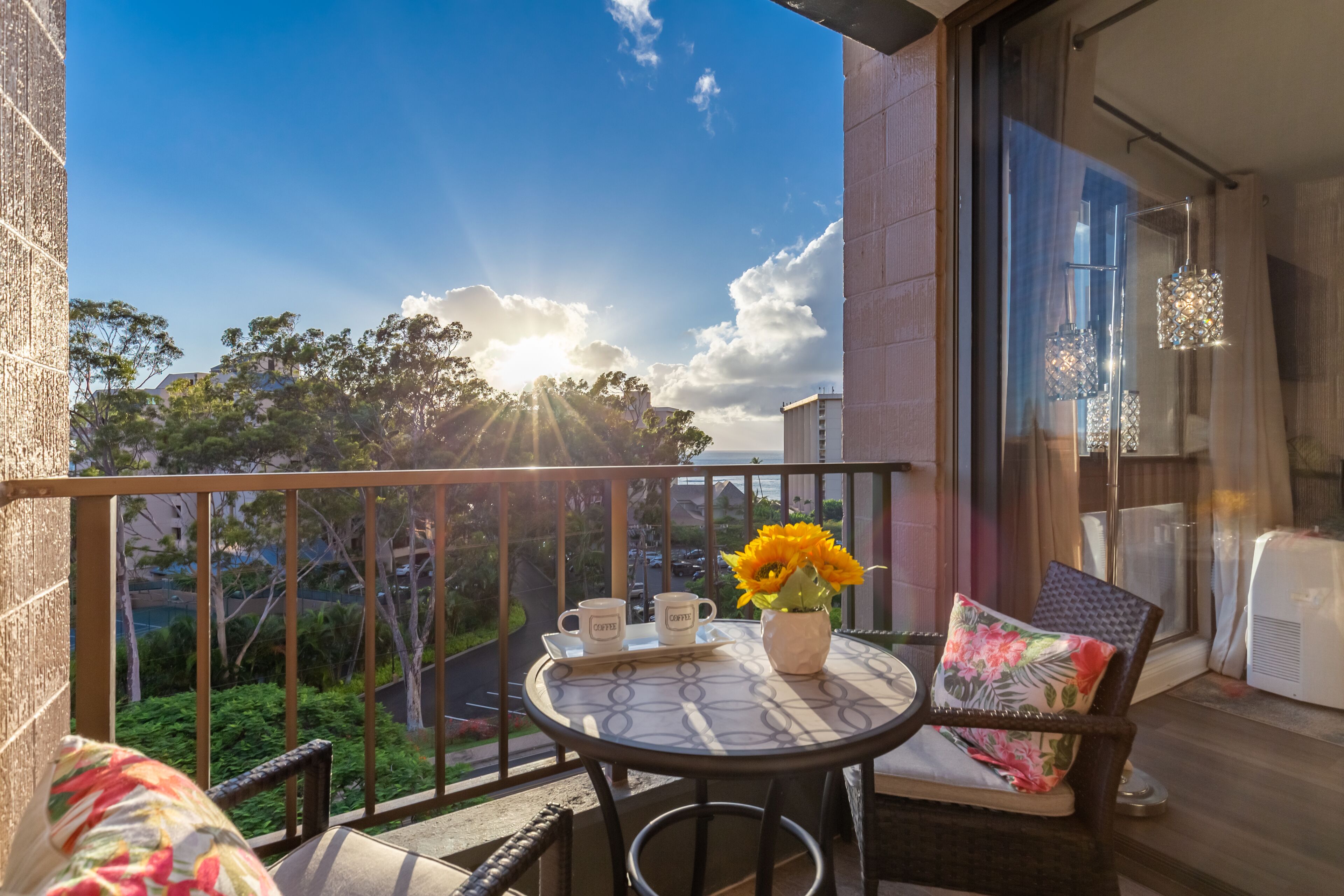 A balcony with a table set for two, a chair, and a potted plant with yellow flowers.