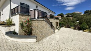 A modern house with a stone facade, a balcony with a glass railing, and a paved driveway. - Villa and private pool - 5 min from the beaches and the city center - car rental (Bastia)