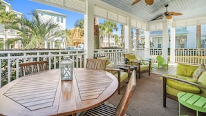A covered outdoor seating area with a round wooden table, chairs, and a ceiling fan. - Perfect home for multiple families with beach tram service and a huge pool. (Inlet Beach, FL)