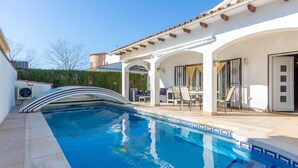 A swimming pool with a curved edge, a covered patio area with outdoor furniture, and a white building with a tiled roof. - Stunning private villa for 6 people with WIFI, A/C, private pool, TV, patio and pets allowed (Castelló D'empúries)