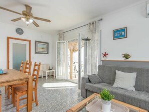 A living room with a wooden dining table, grey sofa, and a ceiling fan.
