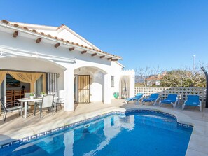 A swimming pool with blue tiles, a covered patio area with a table and chairs, and a view of the surrounding landscape.