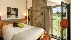 A bedroom with a bed, a stone wall, a balcony with a view of greenery, and a painting on the wall. - Beautiful apartment for 5 guests with WIFI, pool, TV, terrace and pets allowed (Les Vans)