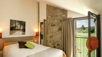 Une chambre à coucher avec un lit, un mur en pierre, un balcon donnant sur un paysage verdoyant et un tableau accroché au mur.