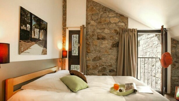 A bedroom with a large bed, stone wall, and a view through a window. - Beautiful apartment for 5 guests with WIFI, pool, TV, terrace and pets allowed (Les Vans)