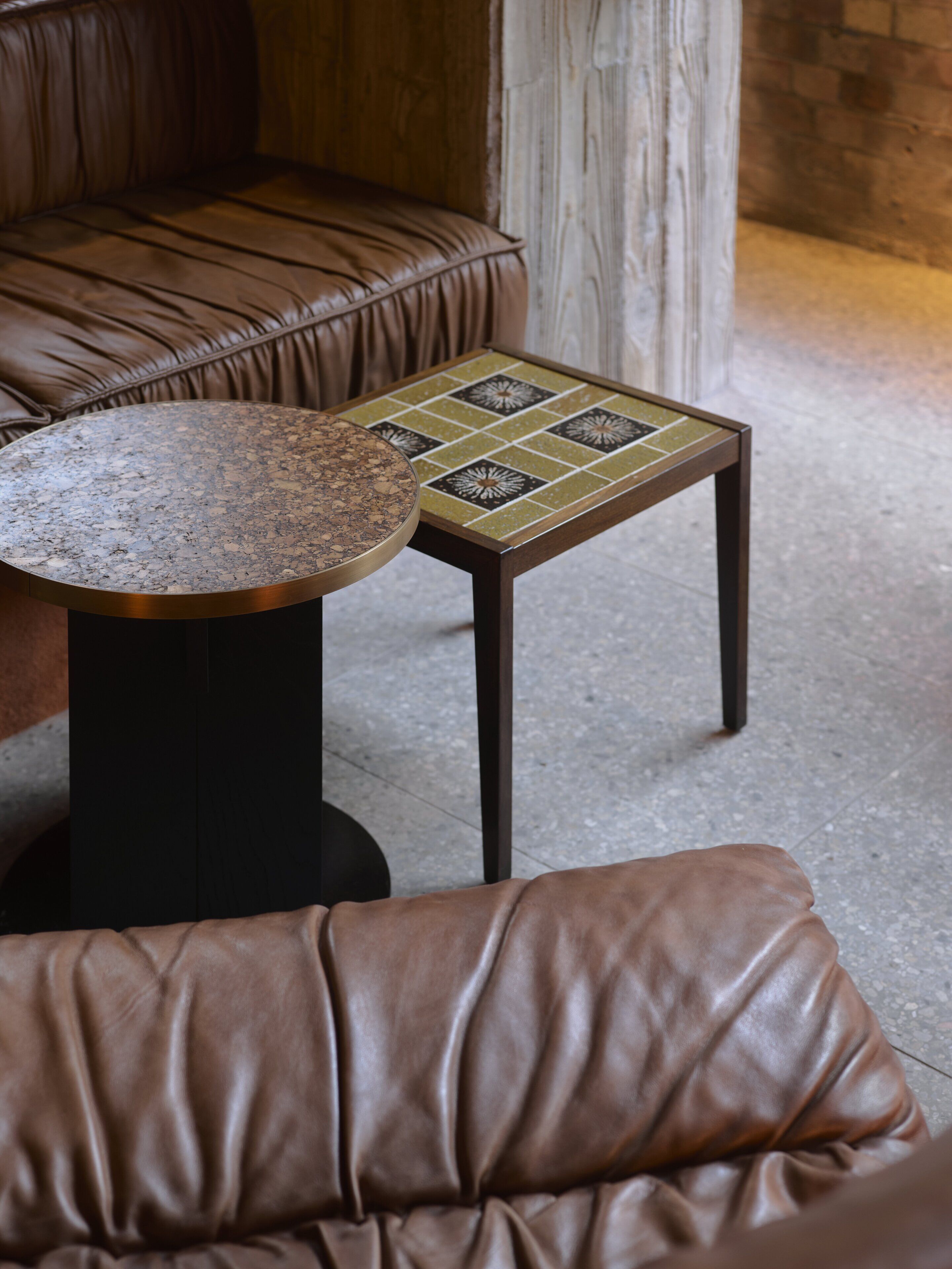 A brown leather sofa and a small round table with a mosaic tile top.