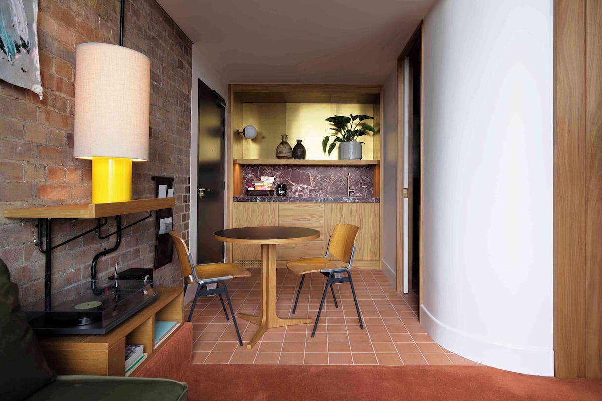 A compact living space with a dining area, a kitchen with wooden cabinets, and a brick wall.