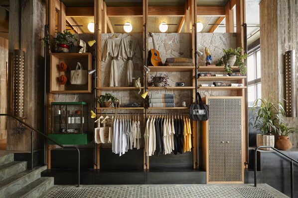A boutique hotel lobby with wooden shelving, a variety of clothing items, and a staircase. - Ace Hotel Sydney (Sydney)