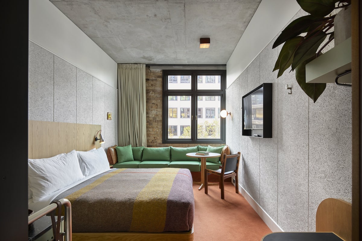A hotel room with a bed, a green sofa, a small table, and a TV mounted on the wall.
