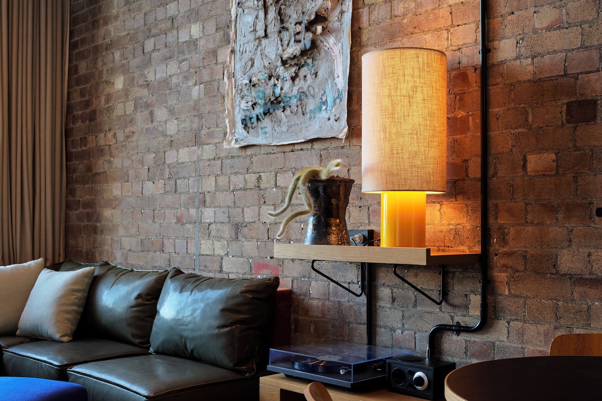 A modern living room with a brick wall, a leather sofa, a wooden dining table, and a lamp.