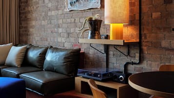 A modern living room with a brick wall, a leather sofa, a wooden dining table, and a lamp.