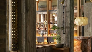 A bar area with wooden beams, a seating area, and a display of bottles. - Ace Hotel Sydney (Sydney)