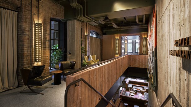 A modern interior with exposed brick walls, wooden paneling, and a mezzanine level with seating. - Ace Hotel Sydney (Sydney)