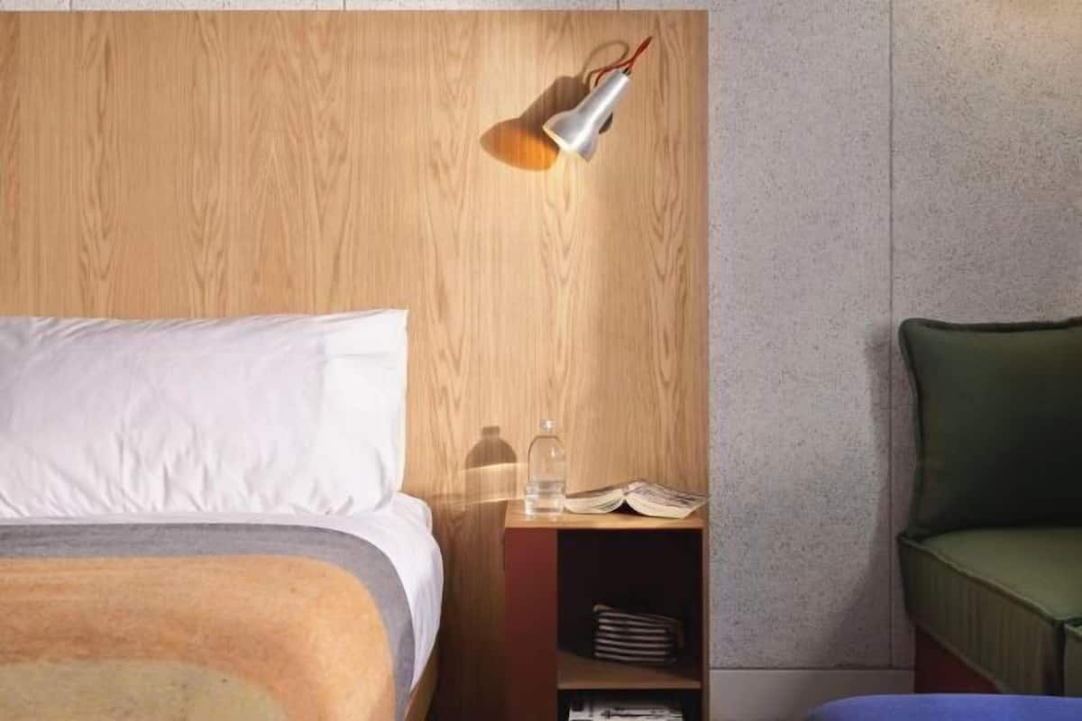 A bedroom with a wooden headboard, a bedside table with a lamp, a green chair, and a bed with white bedding.