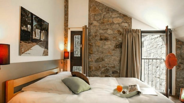 Ein Hotelzimmer mit einem großen Bett, einer Steinwand, einem Balkon mit Blick und einem Bild an der Wand.