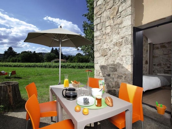 An outdoor dining area with a table set for two, a table umbrella, and a stone wall in the background.