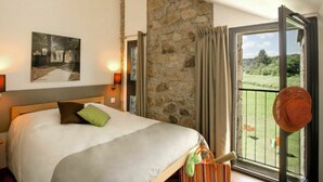 Ein Schlafzimmer mit einem großen Bett, einer Steinwand, einem Balkon mit Blick auf Grünflächen und einem Gemälde an der Wand.