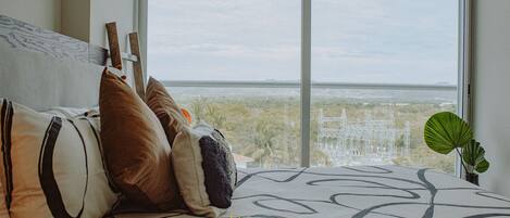 A bed with a view of a cityscape through a large window.