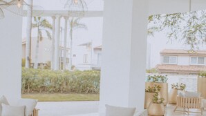 Ein großzügiger Innenbereich mit modernen Möbeln, darunter Sofas und Sessel, und Blick auf einen Garten sowie Gebäude.
