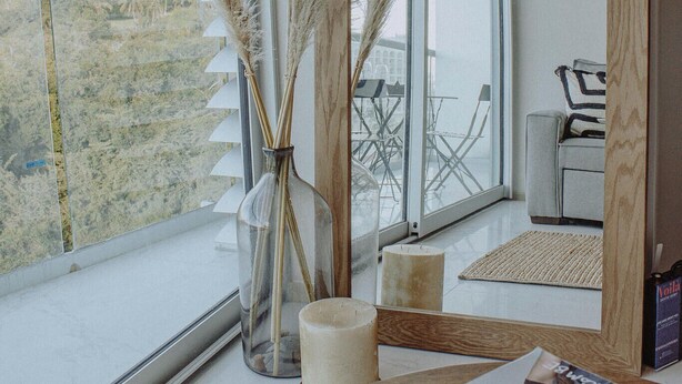 Ein modernes Zimmer mit großem Fenster, einem Spiegel, Pampasgras, einer Zeitschrift und einem kleinen Tisch.