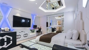A modern hotel room with a large bed, a desk, a flat-screen TV, and a bathroom visible through a glass door. - Theban Hotel (Chungju)