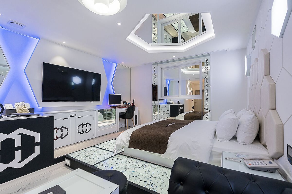 Een moderne hotelkamer met een groot bed, een bureau, een flatscreen televisie en een badkamer zichtbaar door een glazen deur.