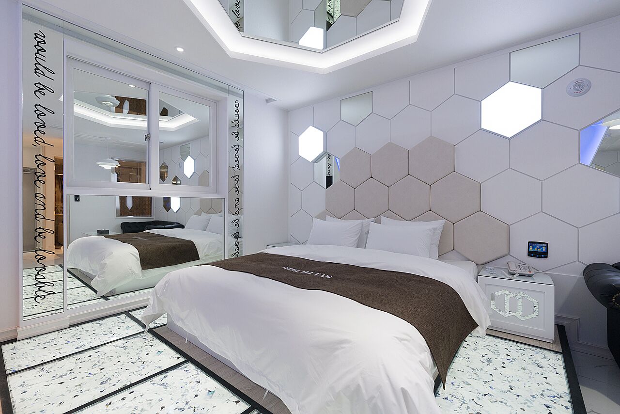 A modern hotel room with a large bed, a nightstand, and a mirror.