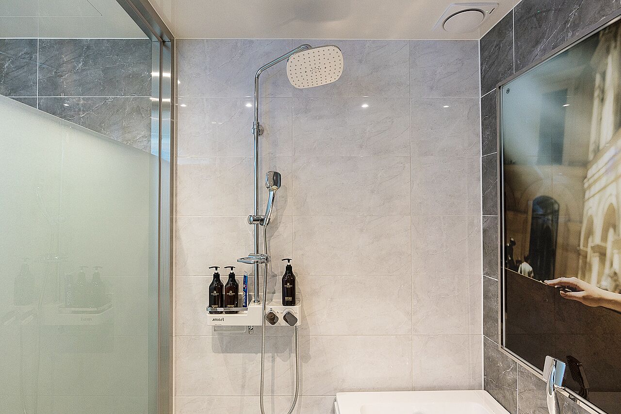 A modern bathroom with a glass shower enclosure, a handheld showerhead, and a wall-mounted faucet.