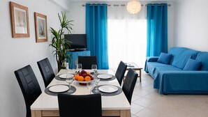 A modern living room with a dining area, blue curtains, a flat-screen TV, and a sofa.