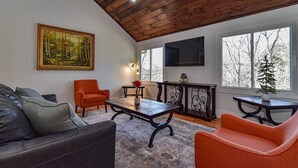 Ein Wohnzimmer mit Holzboden, einem Gemälde an der Wand, einem Sofa, einem Couchtisch und einem Fernseher.