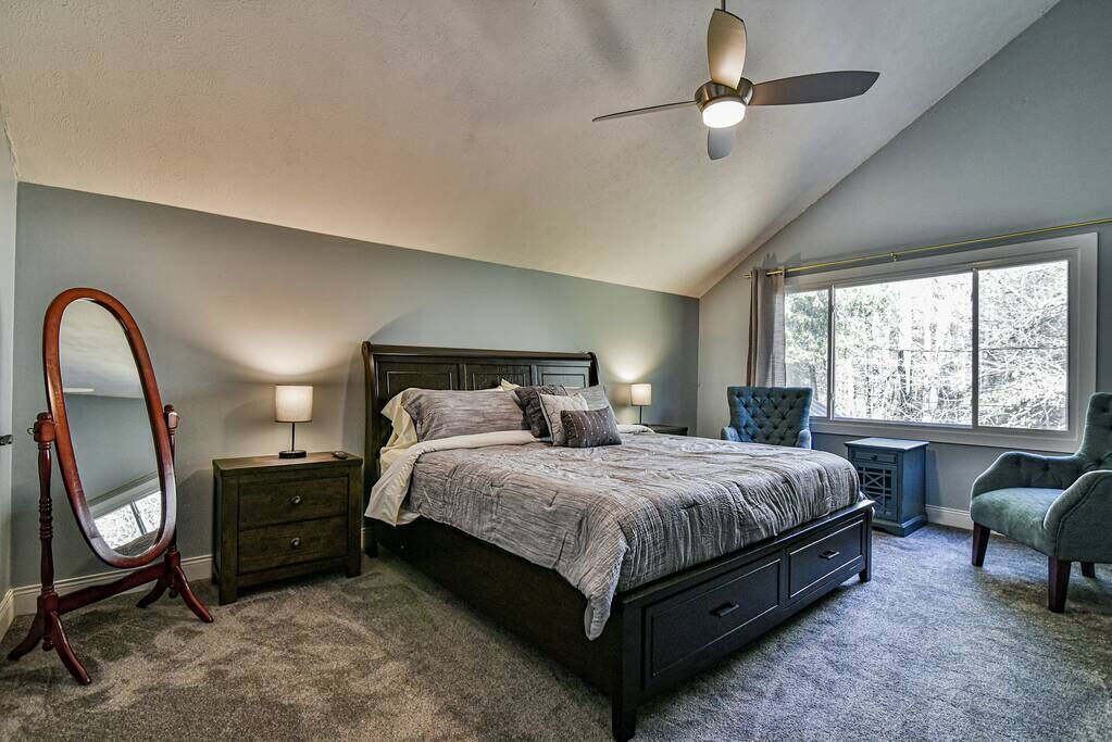 Une chambre à coucher avec un lit, un ventilateur de plafond, une grande fenêtre et un miroir.