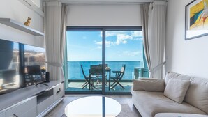 Un salon moderne doté d’un grand téléviseur, d’un canapé, d’une table basse ronde et d’un balcon offrant une vue sur la mer.