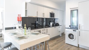 Une cuisine moderne avec des meubles blancs, un four à micro-ondes encastré et un lave-linge.