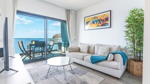 Un salon moderne avec un canapé, une table basse et une grande fenêtre donnant sur la mer.