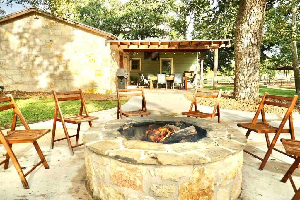 Un hogar de piedra con sillas de madera dispuestas alrededor, un patio cubierto y un edificio de piedra al fondo.