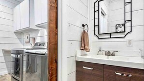 A compact bathroom with a washing machine, a sink with a mirror, and wooden cabinets.