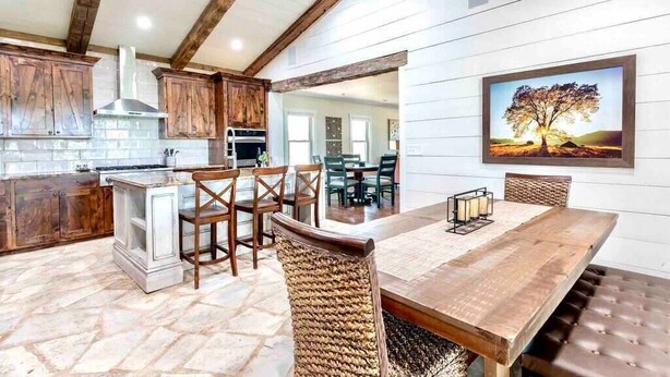 A kitchen with wooden cabinets, a stone floor, and a dining area with a wooden table and chairs.