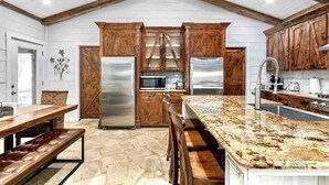A kitchen with wooden cabinets, stainless steel appliances, a granite countertop, and a stone floor.