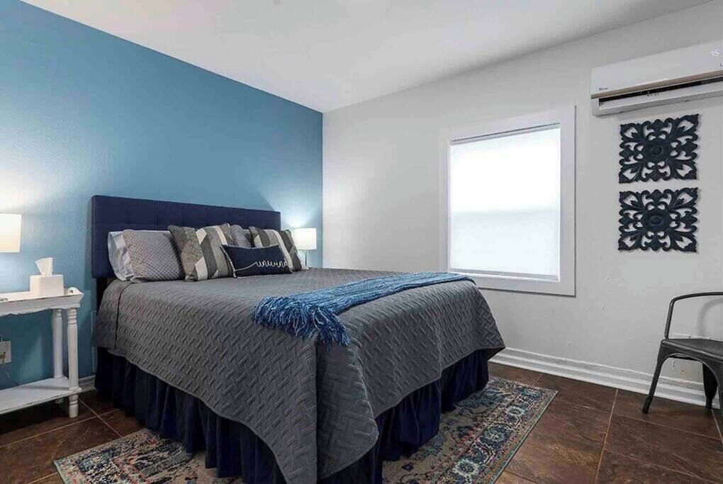 A bedroom with a bed, a nightstand, a chair, a window, and decorative wall art.