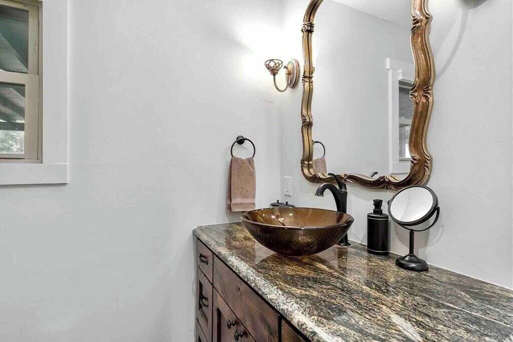 Un baño con un lavamanos ovalado grande, un mueble de tocador de madera, un espejo con un marco ornamentado y un perchero para toallas.