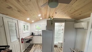 A compact kitchen with a refrigerator, sink, and wooden ceiling.