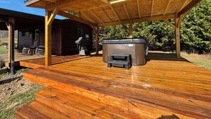 A covered wooden deck with a hot tub and outdoor seating area.