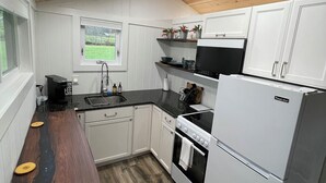 A compact kitchen with white cabinets, a black countertop, and a wooden ceiling.