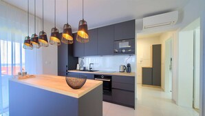 Une cuisine moderne dotée d’un îlot central, de luminaires suspendus et offrant une vue sur l’extérieur.
